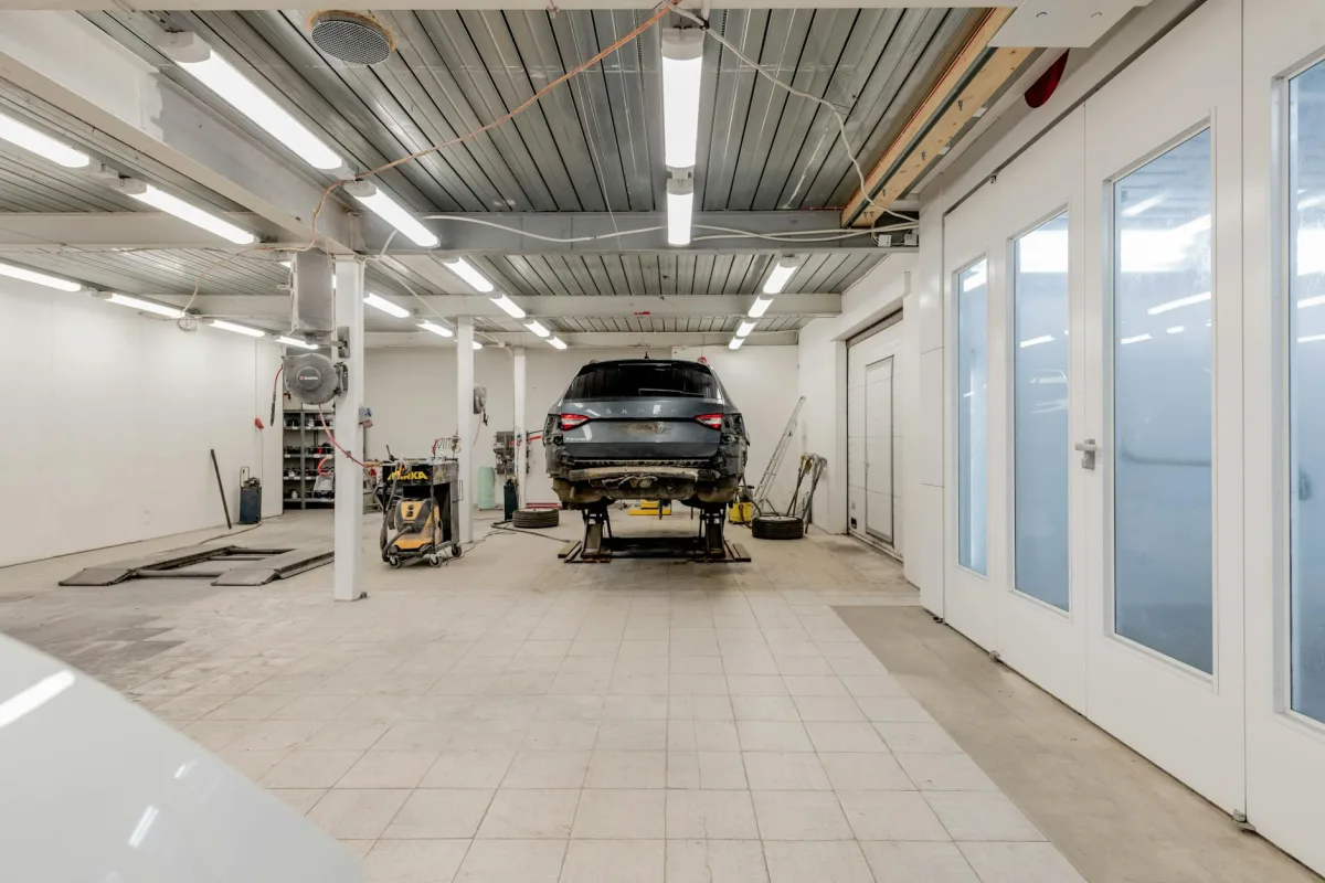 A car parked in an attached garage with the driver-side door open, faint exhaust vapor visible at the tailpipe.