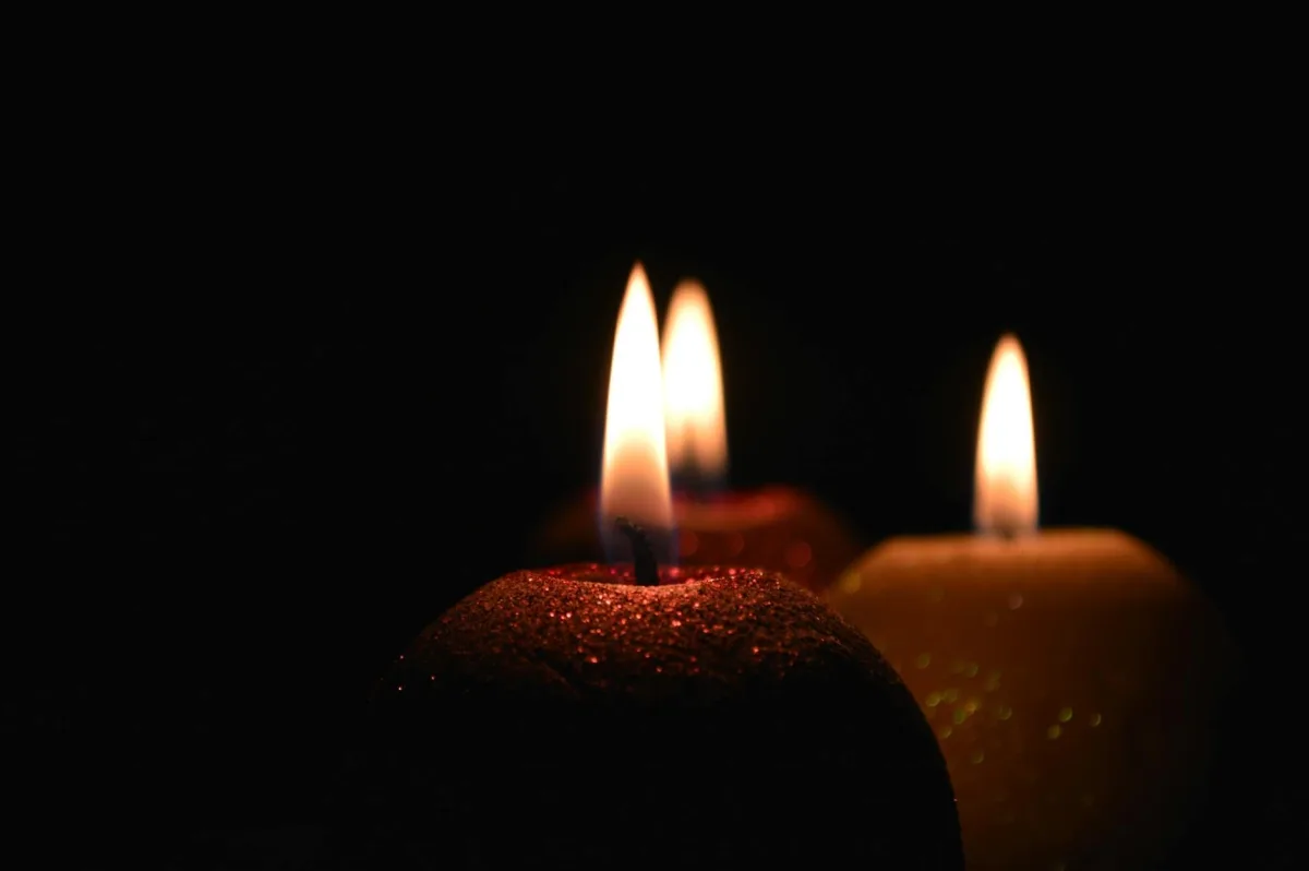 A lit beeswax candle on a wooden table, soft halo of smoke visible above the flame.