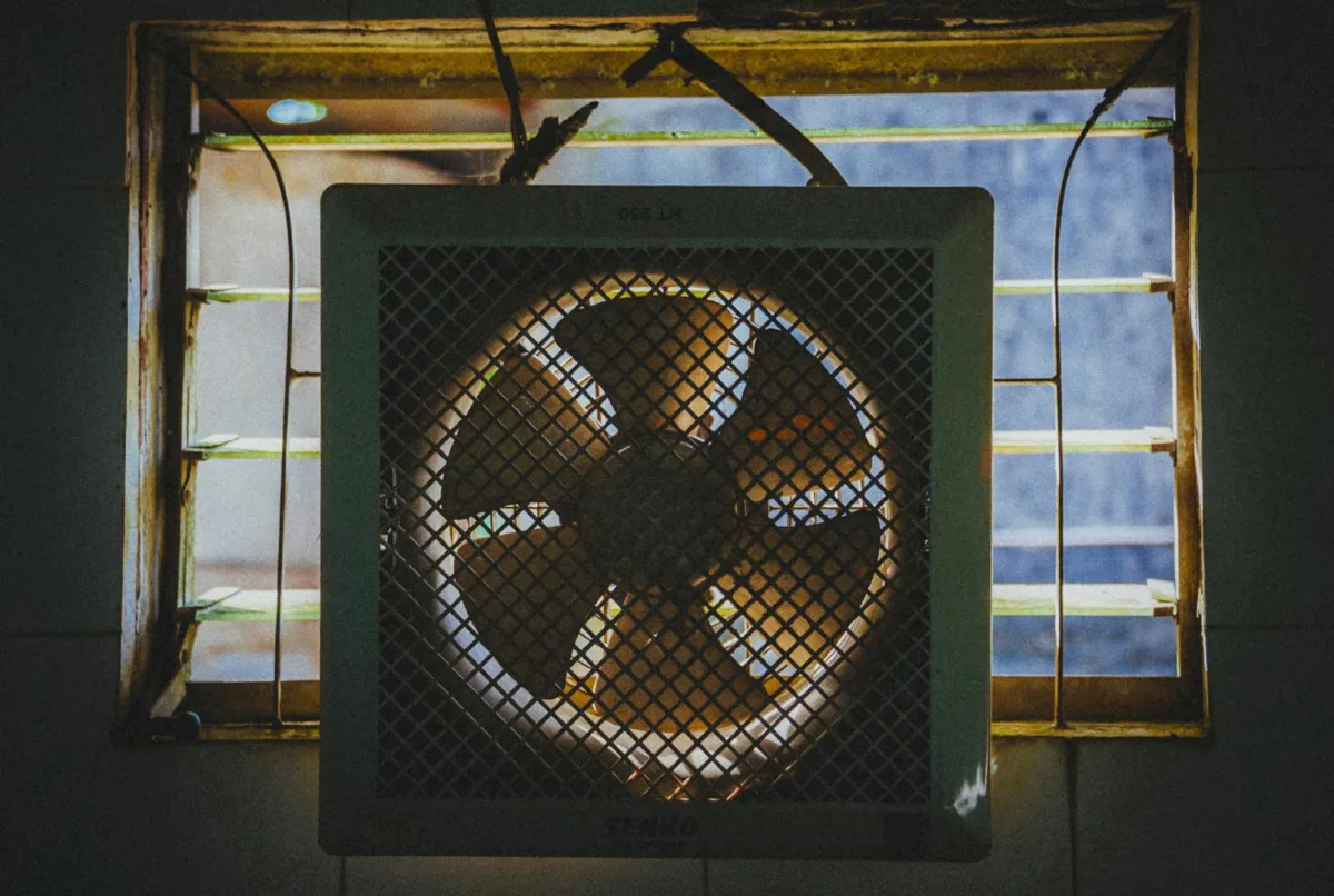 A homemade box-fan air filter, a 20-inch fan with MERV-13 furnace filters taped into a cube shape, in the corner of a living room.