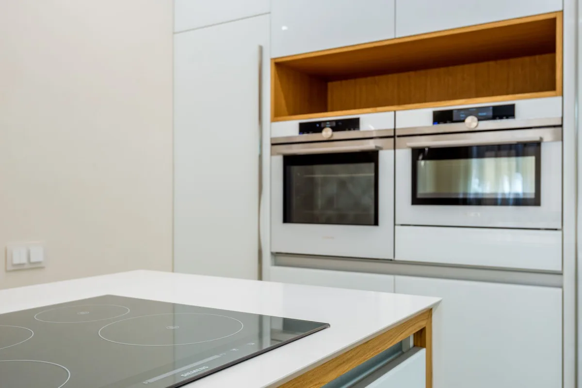 A side-by-side kitchen and utility room showing a gas range and gas water heater on the left, and an induction range, heat-pump water heater, and ducted heat pump on the right.