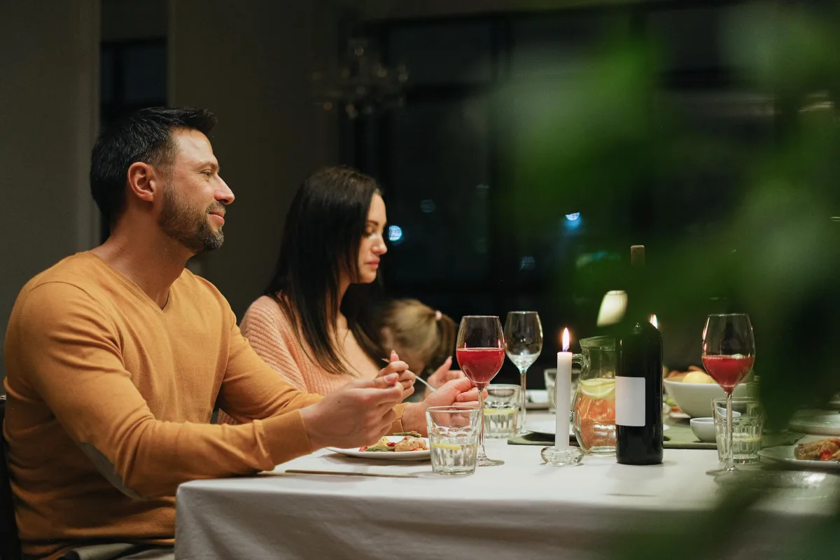 A dining table set for a holiday meal with several lit candles and a fireplace in the background.