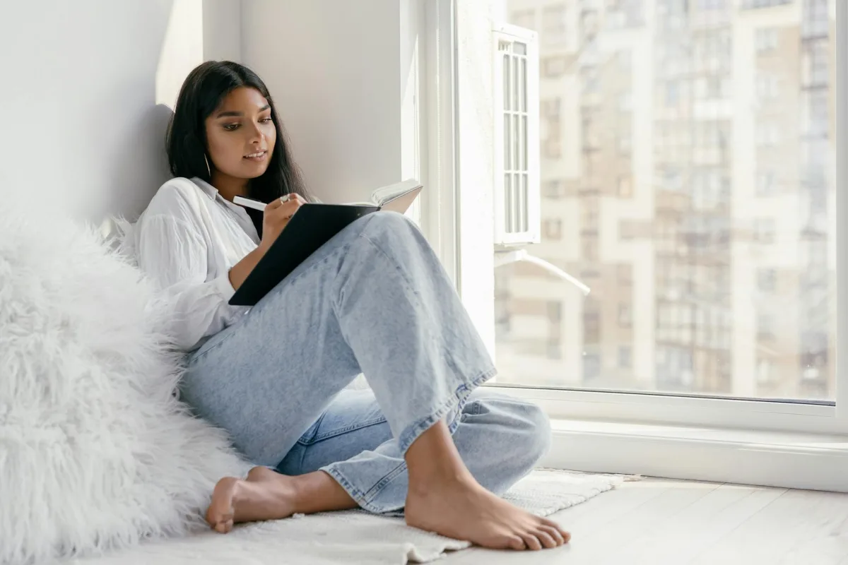 A person at a kitchen table journaling next to a window with a hazy outdoor view, with a Terrestream sensor on the counter.