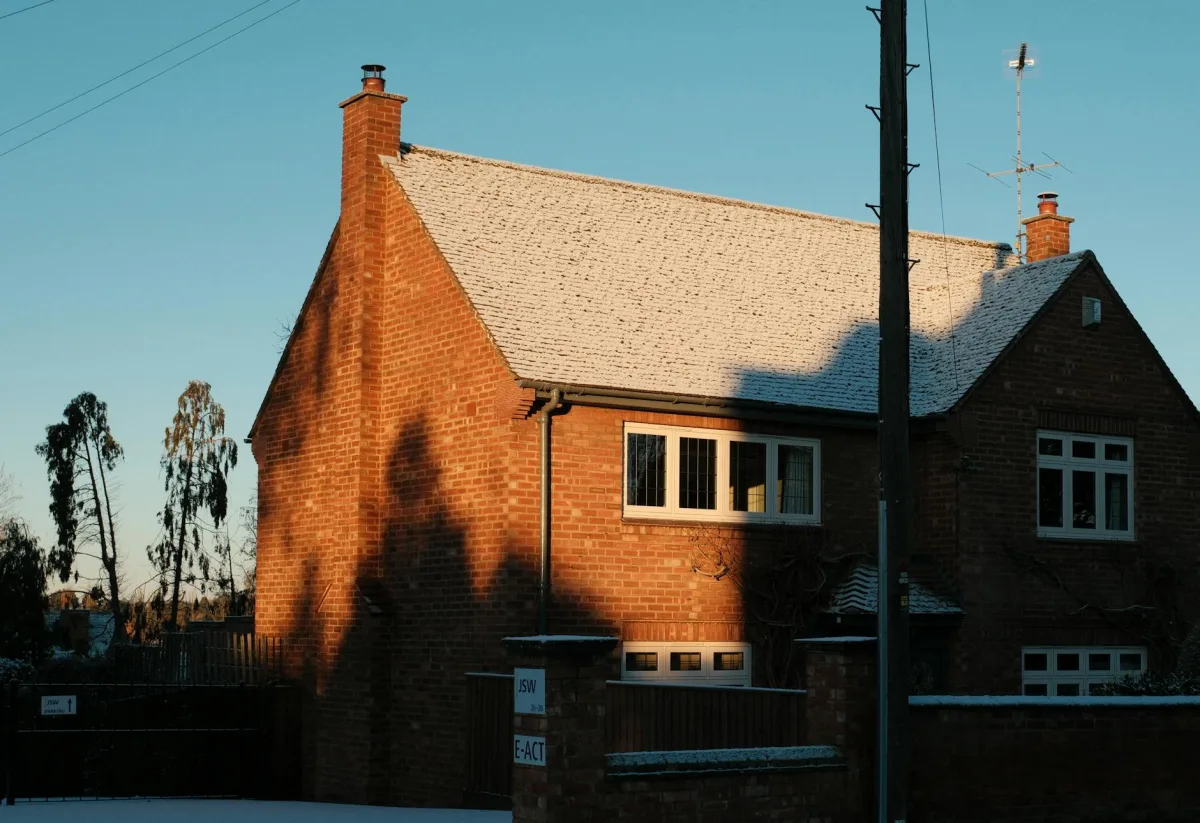 A two-panel cutaway of a three-story house showing winter stack effect (cold infiltration low, warm exfiltration high) and the reversed summer-AC pattern, with arrows tracing the airflow loop.