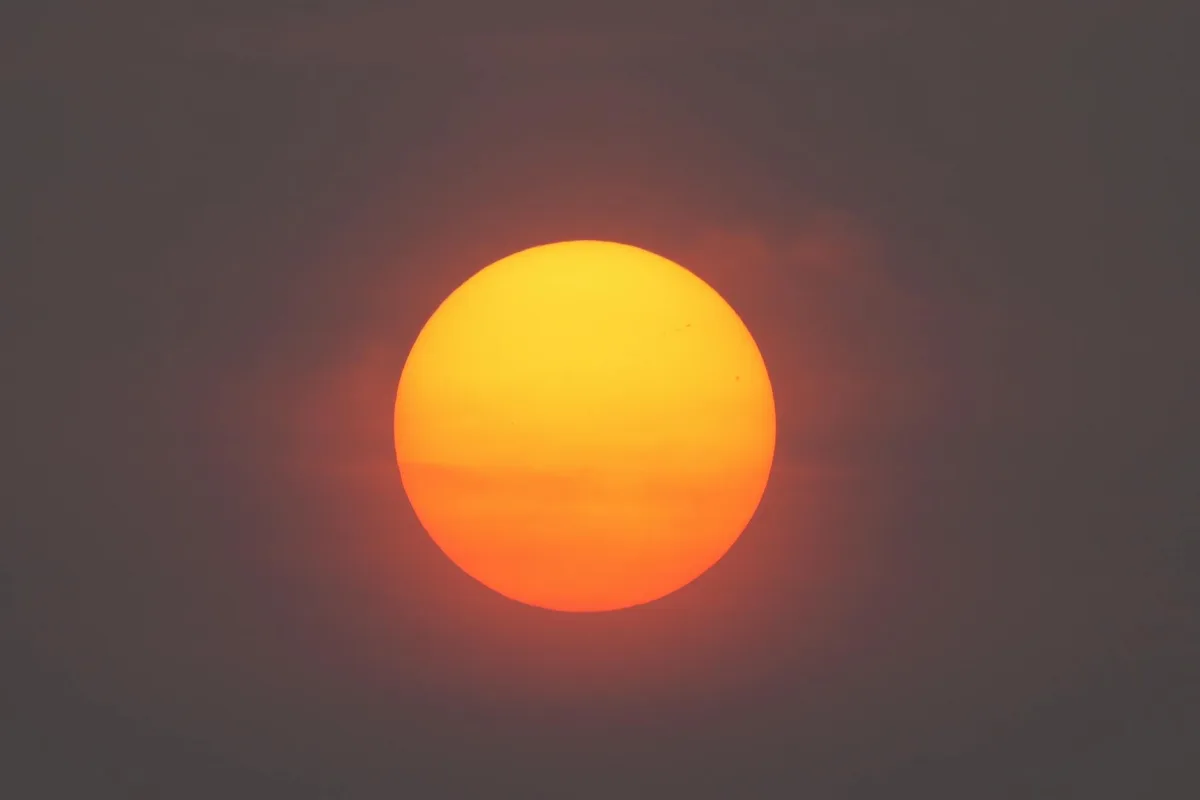 A residential street under thick orange haze, the sun visible as a pale disc through the smoke.