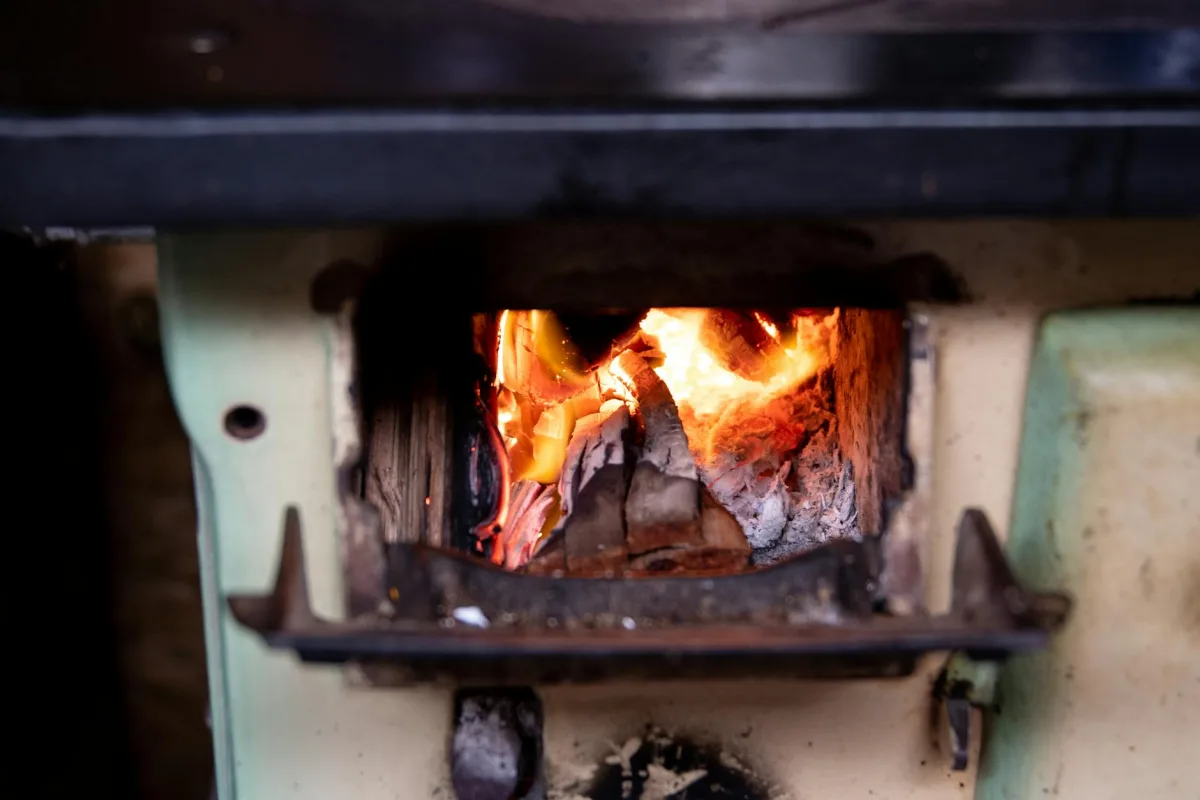 Glowing logs inside a residential wood stove, embers and orange light visible behind the glass.
